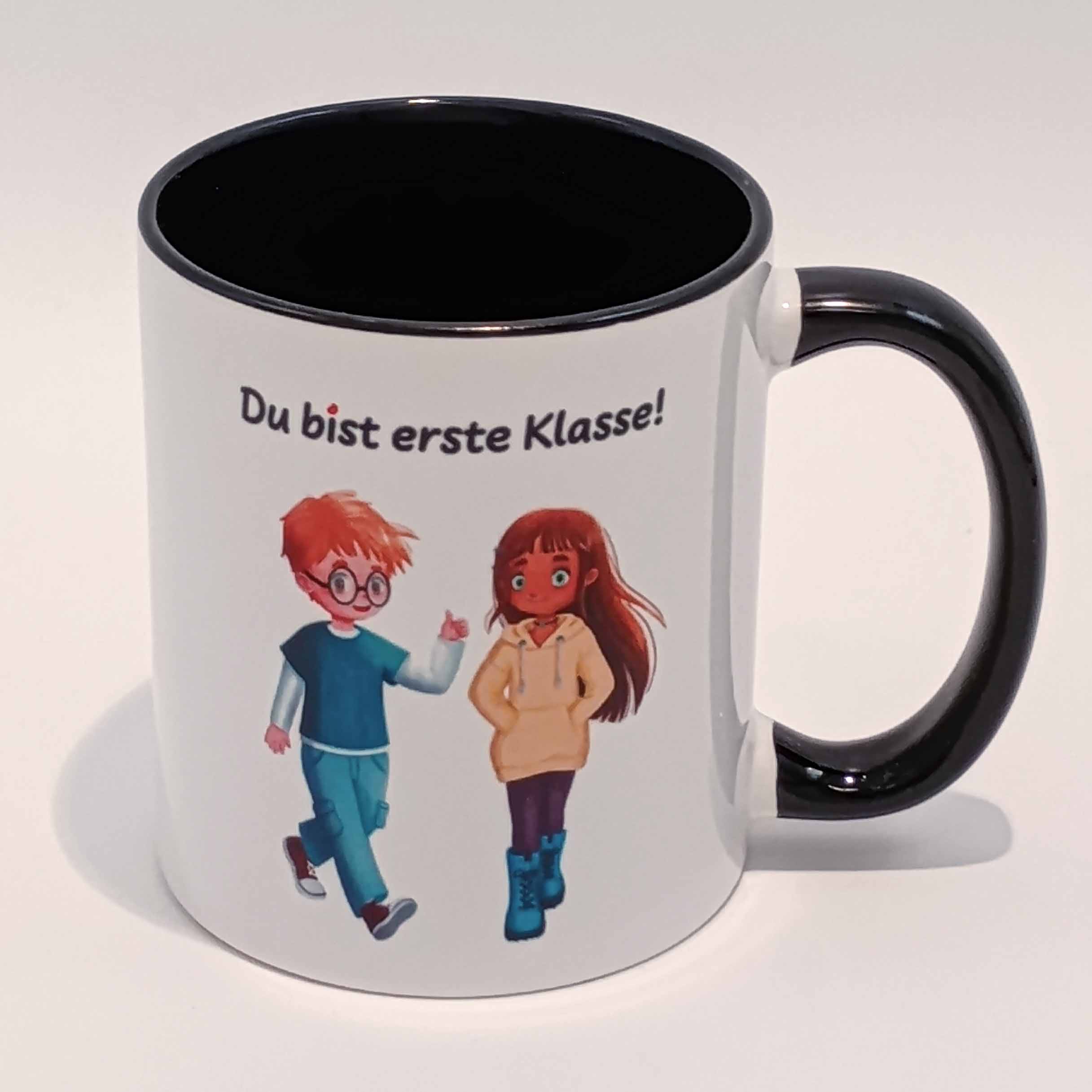Tasse Du bist erste Klasse! Ella und Tim 2 Eine weiße Tasse mit schwarzem Henkel und Innenraum. Darauf abgebildet sind Ella und Tim aus der gleichnamigen Comicreihe mit der Aufschrift "Du bist erste Klasse!" über ihren Köpfen. Die Schrift ist schwarz. Nur der eine i Punkt ist rot. Das Motiv und der Spruch sind auf beiden Seiten jeweils einmal abgedruckt. Die Tasse steht auf weißem Hintergrund und der Henkel zeigt nach rechts.