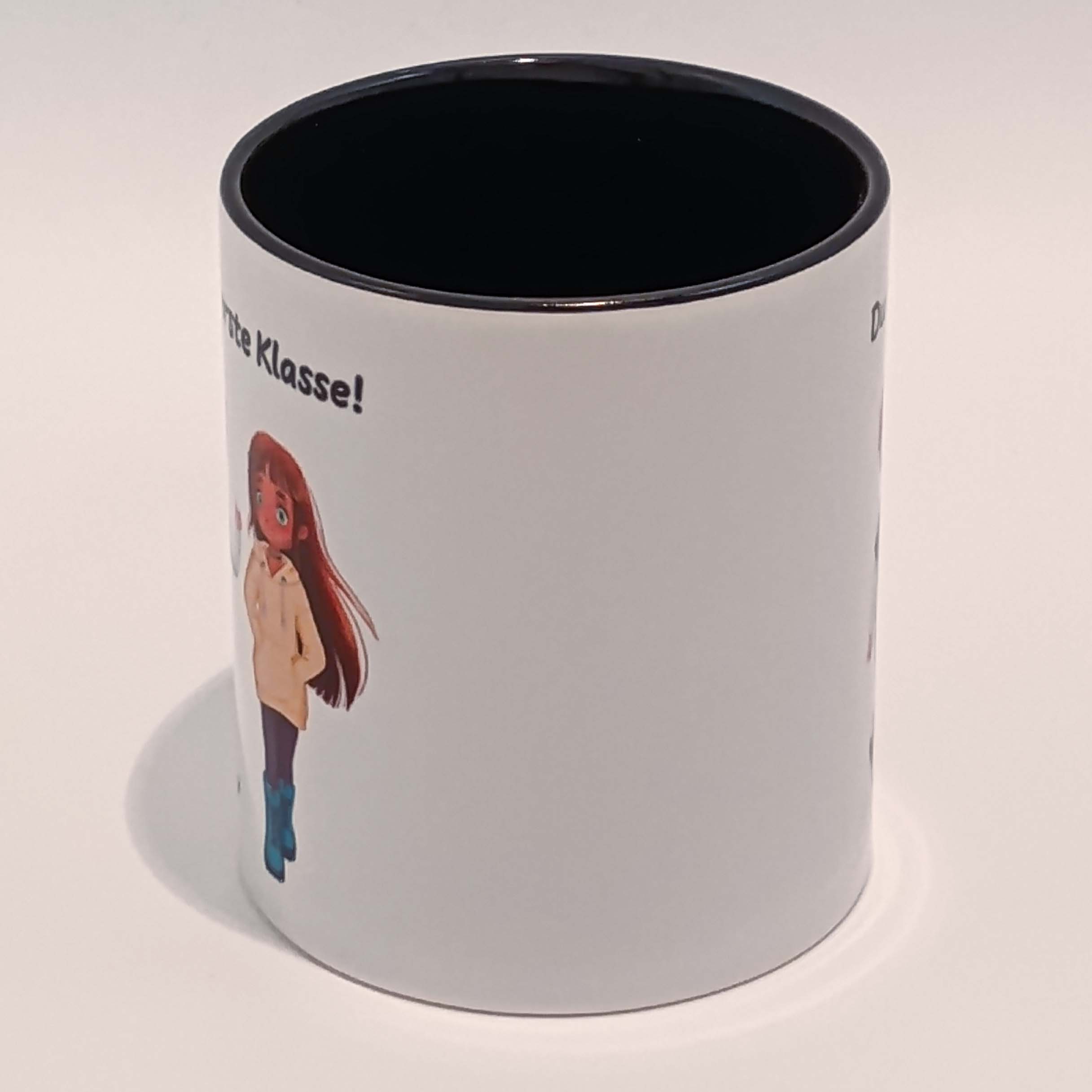 Tasse Du bist erste Klasse! Ella und Tim 4 Eine weiße Tasse mit schwarzem Henkel und Innenraum. Darauf abgebildet sind Ella und Tim aus der gleichnamigen Comicreihe mit der Aufschrift "Du bist erste Klasse!" über ihren Köpfen. Die Schrift ist schwarz. Nur der eine i Punkt ist rot. Das Motiv und der Spruch sind auf beiden Seiten jeweils einmal abgedruckt. Die Tasse steht auf weißem Hintergrund und der Henkel zeigt weg.