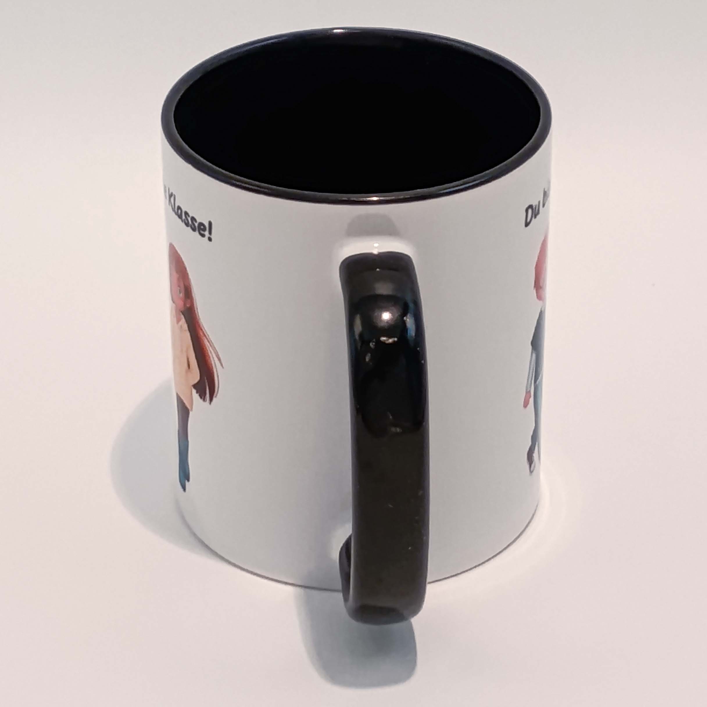 Tasse Du bist erste Klasse! Ella und Tim 3 Eine weiße Tasse mit schwarzem Henkel und Innenraum. Darauf abgebildet sind Ella und Tim aus der gleichnamigen Comicreihe mit der Aufschrift "Du bist erste Klasse!" über ihren Köpfen. Die Schrift ist schwarz. Nur der eine i Punkt ist rot. Das Motiv und der Spruch sind auf beiden Seiten jeweils einmal abgedruckt. Die Tasse steht auf weißem Hintergrund und der Henkel zeigt zu uns.