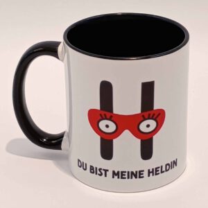 Eine weiße Tasse mit schwarzem Henkel und Innenraum. Darauf das große H mit der Augenbinde vom Edition Helden Logo und der Spruch "Du bist meine Heldin!" in schwarzen Großbuchstaben. Das Motiv und der Spruch sind auf beiden Seiten jeweils einmal abgedruckt. Die Tasse steht auf weißem Hintergrund und der Henkel zeigt nach links.