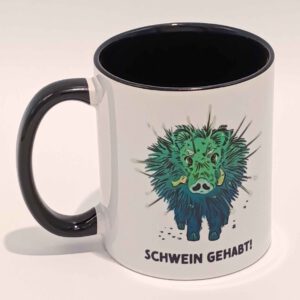 Eine weiße Tasse mit schwarzem Henkel und Innenraum. Darauf ist das Kaktuswildschwein aus dem Kindercomic "Abenteuer im Schattenwald" abgebildet. Das türkis, grüne und sehr stachelige Schwein starrt uns frontal an. Unter seinen Hufen steht schwarz in Großbuchstaben: Schwein gehabt! Das Motiv ist auf beiden Seiten jeweils einmal abgedruckt. Die Tasse steht auf weißem Hintergrund und der Henkel zeigt nach links.